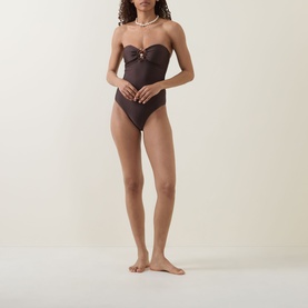 Model wearing dark brown strapless swimsuit with sweetheart neckline and gold ring detail, styled with pearl necklace