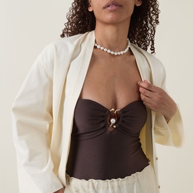 Model wearing dark brown strapless ruched top with gold pearl embellishment, styled with cream blazer and pearl choker necklace