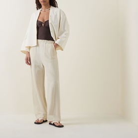 Model wearing cream wide-leg trousers with elasticated waist, styled with matching blazer, brown lace cami and flat sandals