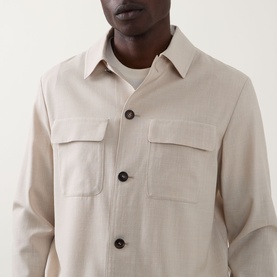 Model wearing Slowear Silk Flap Pocket Overshirt in stone, showing point collar, dark buttons, and twin chest flap pockets, styled over a white tee.