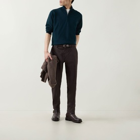 Model wearing John Smedley Tapton Extra Fine Knit Half-Zip Sweater in Richardson green, styled with dark brown trousers and boots, holding a jacket.