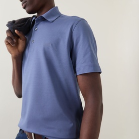 Model wearing Zegna Stitch Logo Polo Shirt in lilac cotton, with classic collar, button placket and short sleeves. Jacket held over shoulder.