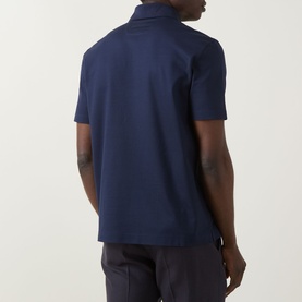 Model wearing Zegna Piquet Polo Shirt in dark indigo, rear view showing short sleeves, straight hem and side vents, styled with grey trousers
