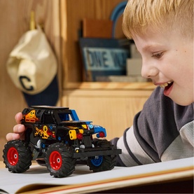 Young child smiling and playing with LEGO Technic Monster Jam Grave Digger Fire and Ice truck, featuring red wheels and flame design