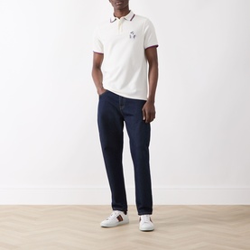 Model wearing Barbour Lure Logo Polo Shirt in Whisper White with navy jeans and white trainers.