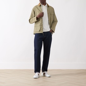 Model wearing Barbour Lure Logo Polo Shirt in Whisper White, styled with a khaki jacket, dark navy jeans, and white trainers.