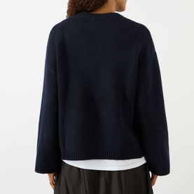 Model wearing Soft Goat navy knit jumper, back view, styled over white shirt with dark trousers.