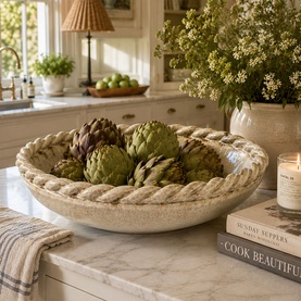 Mindy Browne Risto Decorative Bowl in cream ceramic with rope-twist rim, styled with artichokes on a marble surface.