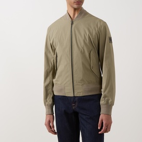 Model wearing Belstaff Carrier Water-Repellent Bomber Jacket in green with ribbed collar, zip fastening and logo badge, styled with navy jeans.