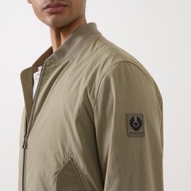 Model wearing Belstaff Carrier Water-Repellent Bomber Jacket in green, showing ribbed collar, zip fastening, and logo badge on sleeve.
