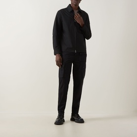 Model wearing Belstaff Compact Technical Cargo Overshirt in black with pointed collar and two-way zip, styled with black trousers and leather shoes.