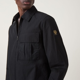 Model wearing Belstaff Compact Technical Cargo Overshirt in black with chest patch pocket, two-way zip and gold logo badge at sleeve.