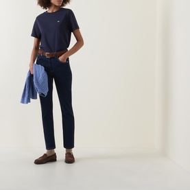 Model wearing Gant Shield Logo T-Shirt in navy with dark jeans and brown loafers, holding a light blue shirt