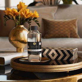 Rituals Velvet Oudh Refill Home Perfume bottle on a gold tray with decorative box and yellow flowers in a warm living room setting.