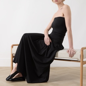 Model wearing Part Two Balina Flared Dress in black; strapless midi with fitted bodice and flared skirt, styled with black flat shoes