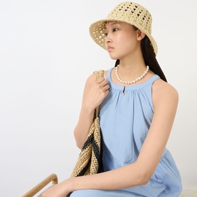 Model with Part Two Beinta Woven Bucket Hat in natural paper, wide brim, open-weave crown; styled with pearl necklace and woven bag