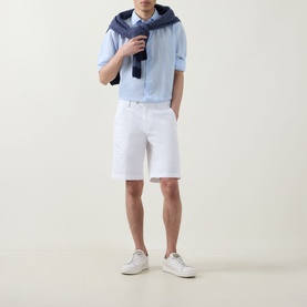 Model wearing Boggi Milano white cotton-elastane shorts with light blue shirt, navy jacket draped over shoulders, and white trainers.