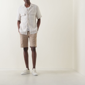 Model wearing Boggi Milano Slim-Leg Bermuda Shorts in Mud, styled with a white short-sleeve shirt and white slip-on trainers.