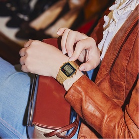 Model with Casio Vintage A159WGEA-1EF gold-tone digital watch, styled with tan leather jacket and red clutch bag