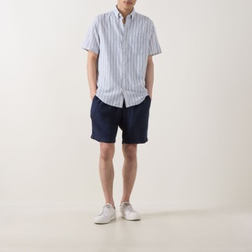Model wearing Gant Reg Shirt in vintage blue vertical stripe linen-cotton blend, styled with navy shorts and white trainers.