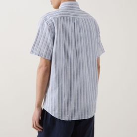 Model wearing Gant Reg Shirt in vintage blue stripe linen-cotton blend, short sleeves, rear view, styled with navy trousers.