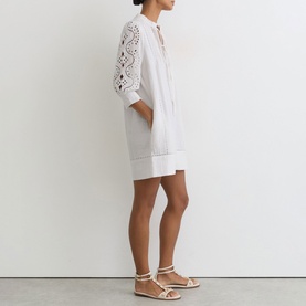 Model wearing Reiss white mini dress with broderie anglaise sleeves and tie neck, styled with gold flat sandals