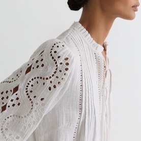 Model wearing Reiss white broderie anglaise blouse with pintuck front, lace-up neckline and scalloped cutwork sleeves