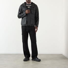 Model wearing Rains black casual jacket with chest pockets, styled with black cargo trousers and dark trainers.