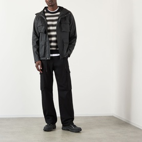 Model wearing Rains black casual jacket with hood, styled with striped knit, black cargo trousers and chunky trainers
