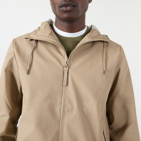 Model wearing Rains beige casual jacket, hooded with zip fastening and drawstring detail, styled with olive crew-neck top
