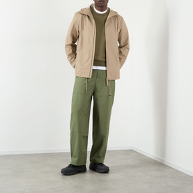Model wearing Rains beige casual jacket, styled with olive hoodie, white tee, and green cargo trousers with black trainers.