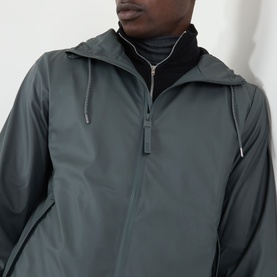 Model wearing Rains Dark Grey casual jacket, hooded with half-zip detail, styled with black roll-neck underneath