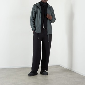 Model wearing Rains Dark Grey casual jacket with black roll-neck, wide-leg black trousers and black chunky trainers.