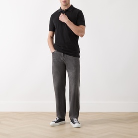 Model wearing Scotch & Soda Logo Piqu&eacute; Polo Shirt in black with grey straight-leg jeans and black low-top trainers