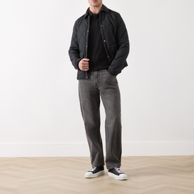 Model wearing Scotch & Soda Logo Piqu&eacute; Polo Shirt in black, styled with dark quilted jacket, grey jeans, and navy trainers