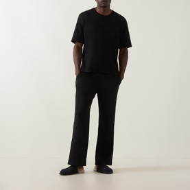 Model wearing Calvin Klein black cotton lounge trousers with matching black T-shirt and dark slip-on shoes.