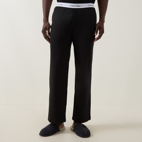 Model wearing Calvin Klein black cotton lounge bottoms with logo waistband, styled with dark slippers