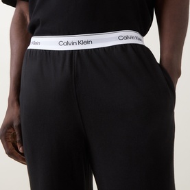 Model wearing Calvin Klein black cotton lounge bottoms with white logo waistband, close-up detail shot.
