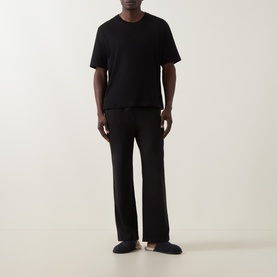 Model wearing Calvin Klein black cotton lounge bottoms with matching black T-shirt and navy slippers.