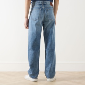 Model wearing Calvin Klein Jeans 90s Mid-Rise Straight Leg Jeans in Andrew blue, five-pocket style, rear view, styled with white trainers.
