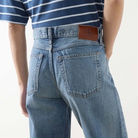 Model wearing Calvin Klein Jeans 90s Mid-Rise Straight Leg Jeans in Andrew blue, showing rear five-pocket detail and leather logo badge.