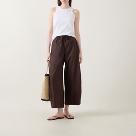 Model wearing InWear Raven Wide-Leg Trousers in dark brown with white sleeveless top, styled with tan sandals and straw tote bag.