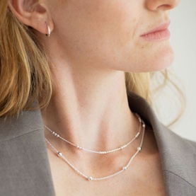 Model with Juvi Essential Huggies in silver sterling huggie-style earrings, styled with layered delicate silver necklaces and grey blazer
