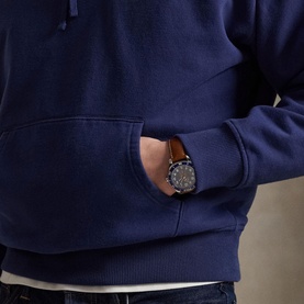 Model wearing Ralph Lauren dark cobalt hoodie with kangaroo pocket, styled with a brown-strapped watch with dark dial.