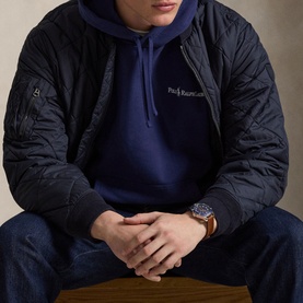 Model wearing Ralph Lauren dark cobalt hoodie, styled with black quilted jacket, jeans, and a brown leather watch.