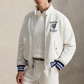 Model wearing white bomber jacket with Wimbledon graphic, blue and white stripe ribbed cuffs and hem, styled with white trousers