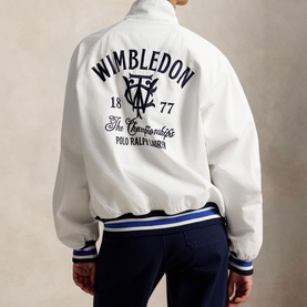 Model wearing white Polo Ralph Lauren Wimbledon bomber jacket with navy graphic back print, ribbed striped hem, paired with navy trousers