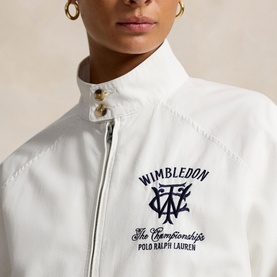 Model wearing white zip-up jacket with navy Wimbledon The Championships graphic on chest, gold hoop earrings visible