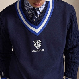 Model wearing Ralph Lauren Wimbledon Logo Hybrid Sweater in Refined Navy with striped V-neck, cable-knit sleeves, over a striped shirt and tie.