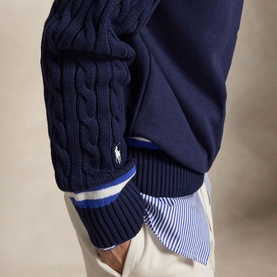 Model wearing Ralph Lauren Wimbledon Logo Hybrid Sweater in Refined Navy with cable-knit sleeves, striped cuffs, layered over a striped shirt with